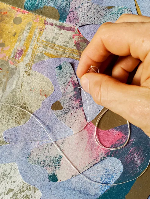 Close up on artist Julien Gardair hand stitching a painting cutout.